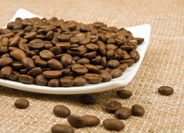 Зерна кофе лежат на блюдце на заднем плане мешка — стоковое фото