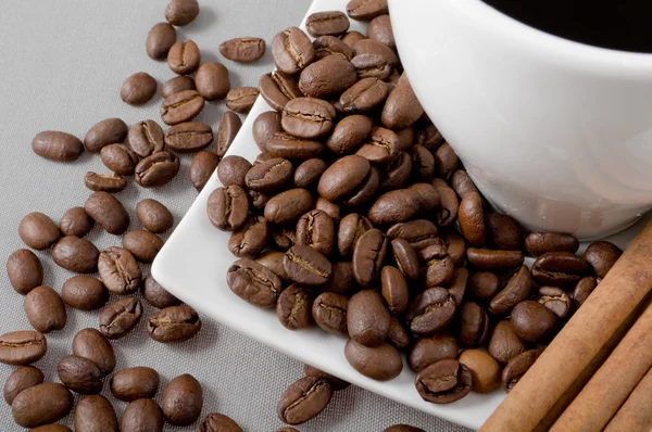 Black coffee, grains and cinnamon on a grey background — Stock Photo, Image