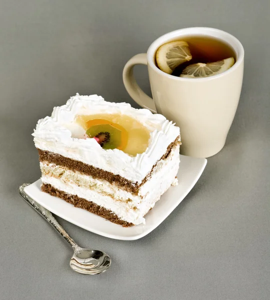 Piece of cake with fruit, tea with a lemon, tea-spoon — Stock Photo, Image