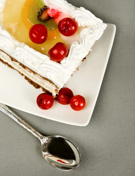 Piece of cake with a cherry on a saucer and tea-spoon — Stock Photo, Image