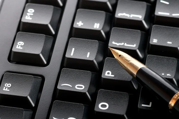 Pen with a golden feather lying on the black keyboard macro — Stock Photo, Image