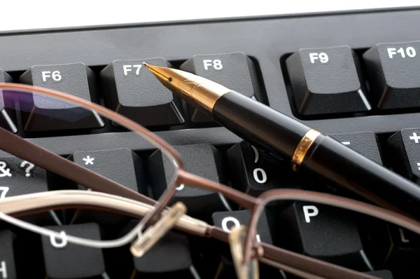 Pen with a golden feather and glasses is on the black keyboard — Stock Photo, Image