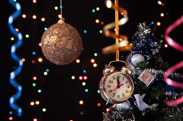 Bola de Natal, relógio, serpentina, uma árvore de Natal decorada sobre um fundo preto com luzes — Fotografia de Stock