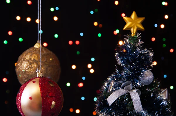 Zwei Weihnachtsbaumkugeln, ein geschmückter Weihnachtsbaum auf schwarzem Hintergrund mit Lichtern — Stockfoto