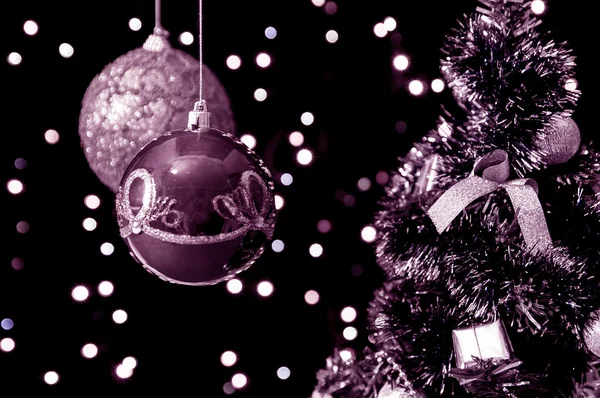 Duas bolas de Natal penduradas em um fundo preto com luzes brilhantes e decorado a árvore de Natal — Fotografia de Stock