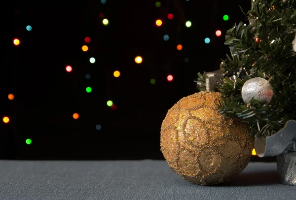 Boule dorée sous un sapin de Noël décoré dans la couleur de fond des lumières — Photo