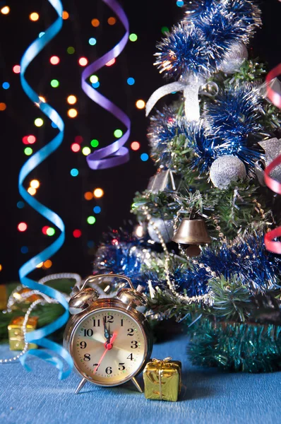 Orologio, palla, serpentino, un albero di Capodanno su sfondo nero con luci — Foto Stock