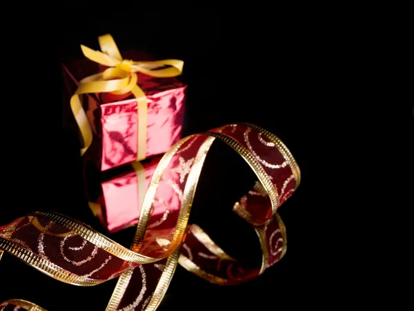 The gift in the red packaging, delicate red ribbon on a black background with reflection — Stock Photo, Image