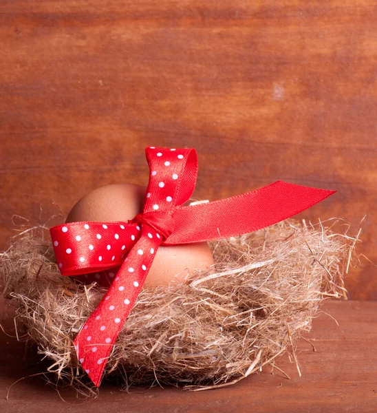 Пасхальне яйце в гнізді з червоною стрічкою на дерев'яному фоні — стокове фото