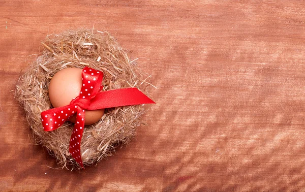 Egg with red bow in the nest on the wooden background — Stock Photo, Image