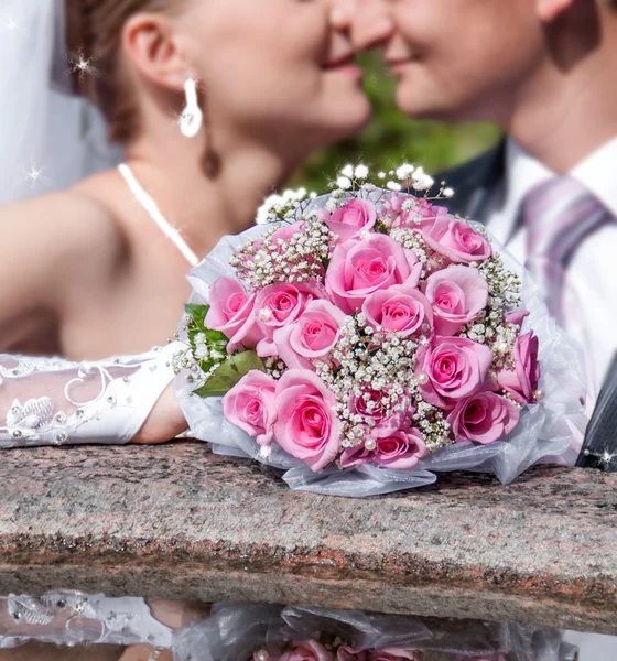 Braut und Bräutigam küssen sich auf dem Hintergrund eines Blumenstraußes — Stockfoto