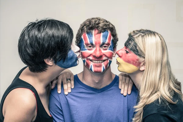 Amigos felices con banderas pintadas en caras besándose — Foto de Stock