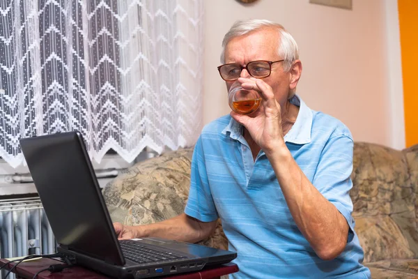 Senior with laptop and glass of whiskey — Stock Photo, Image