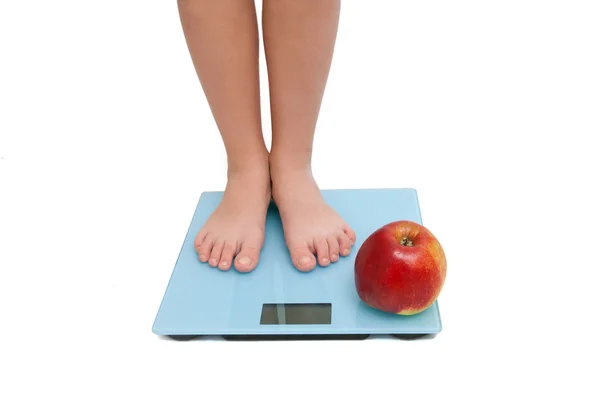 A pair of female legs standing on a bathroom scale with an — Stock Photo, Image