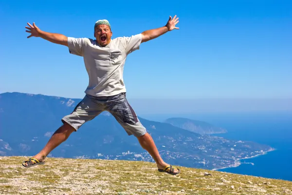 Счастливый человек прыгает на фоне гор, неба и моря — стоковое фото