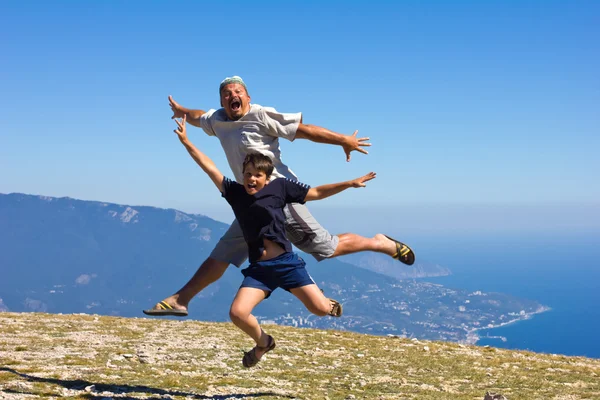 Happy man and boy jumping on a background of mountains and sky a — Stock Photo, Image