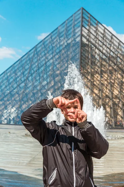 Smiling boy in Paris frame gesturing in front of the Louvre pyra — Stock Photo, Image