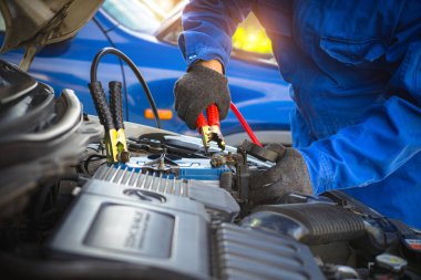 Pili bitmiş araba konsepti. Kırmızı ve siyah kablolarla şarj olan tamirci araba aküsü. Aracın motor gücünü kesiyorum. Garajda takviye kablosu tutan bir adam var..