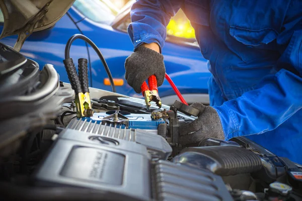 Battery car dead concept. A mechanic repair car battery, charging with red and black cables. fixing vehicle engine power down. Man holding jumper cable in garage.