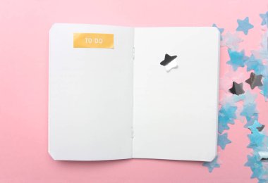 Not defteri ve mavi, beyaz ve gümüş konfeti pembe renkli kağıt arka planda minimal stil.