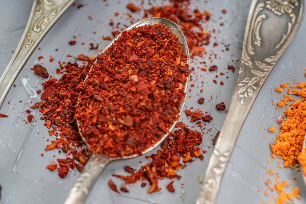 Red chili powder or paprika in a spoon on a gray background, close-up. Cooking ingredients, flavor.