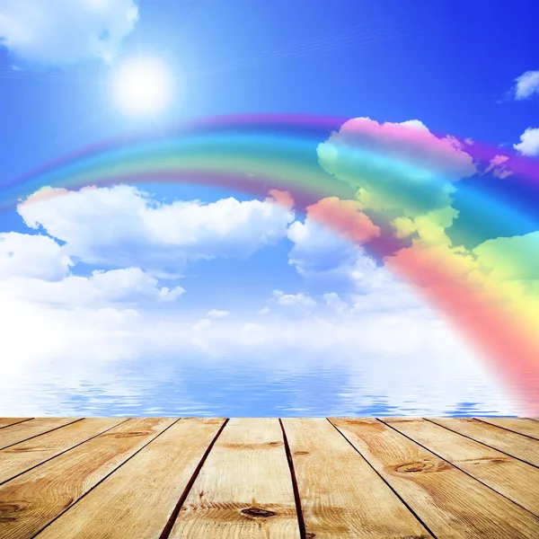 Blue sky background with rainbow and reflection in water. Wood pier — Stock Photo, Image