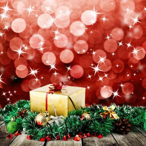 Gouden kerst cadeau doos met kerstballen op houten planken over rode blured achtergrond met licht en sterren — Stockfoto