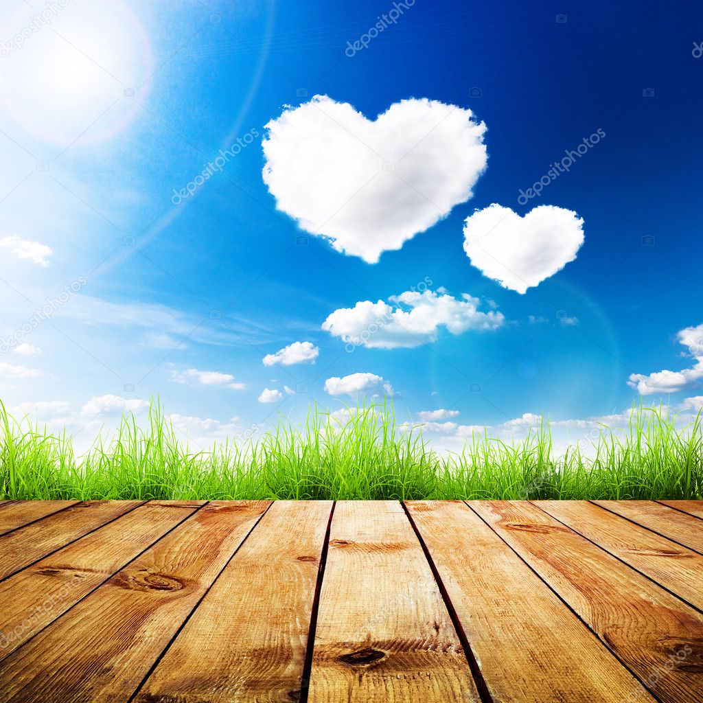 Green grass on wooden plank over a blue sky with hearts shape clouds.