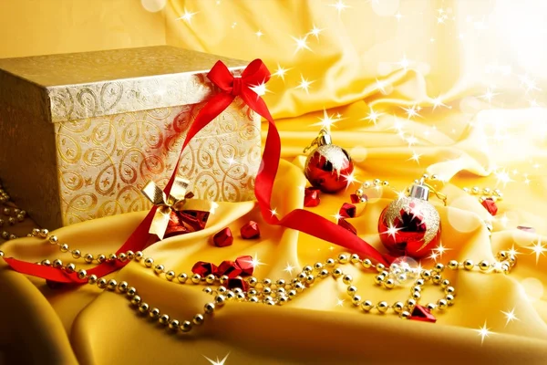 Golden gift with red bow on silk with rays and star. — Stock Photo, Image