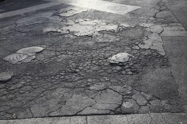 Damaged road surface. Bad road quality with multiple potholes and patches in Paris, France.