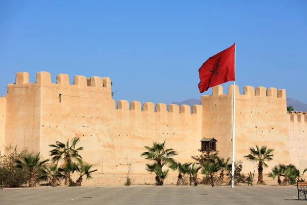 City walls, Moroccan flag and palm trees in Taroudant city, Morocco.