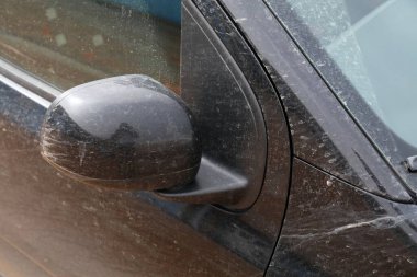 Kirli arabanın yıkanması lazım, üzerinde leke ve yan ayna olan küçük siyah bir araba..