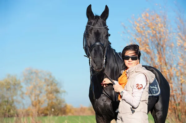 彼の所有者とライダーと美しい黒い馬の肖像画緑の芝生の牧草地にポーズ — ストック写真