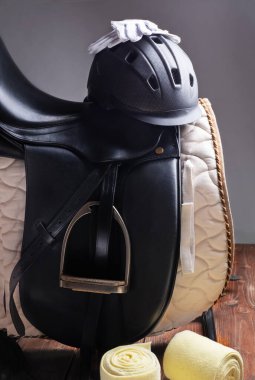 Siyah profesyonel deri eyer, binicilik kaskı ve eyer rafına yerleştirilmiş eldivenlerle birlikte.