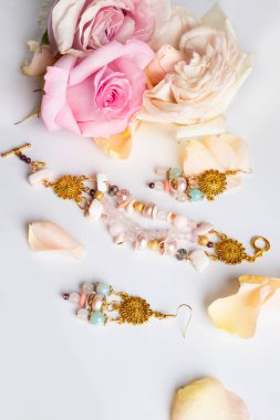 Altın el yapımı mücevher bilezik ve yarı değerli ve beyaz arka planda gül yaprakları.