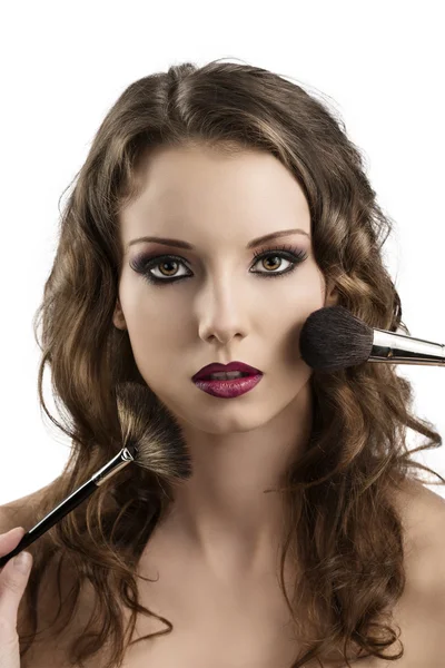 Girl getting made-up with brushes on the face — Stock Photo, Image