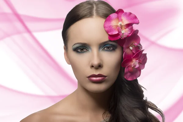 Mooie brunette met bloemen in de buurt van gezicht. bloemen zijn nep — Stockfoto