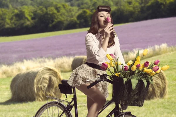 Porträtt av vintage pin-up på cykel att lukta en blomma i landsbygdens co — Stockfoto