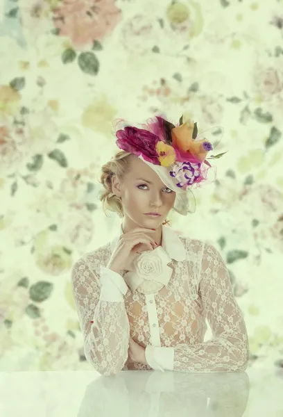 Elegante ragazza dietro il tavolo con cappello floreale e mano sotto il chi — Foto Stock