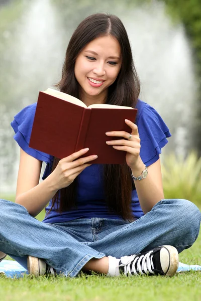 Mulher bonita lendo um livro no parque com sorriso — Fotografia de Stock