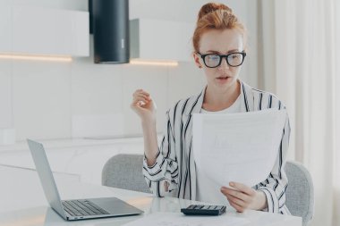 Meşgul kızıl saçlı kadın finansör iş dünyasının mali muhasebe hesaplarını yapıyor.