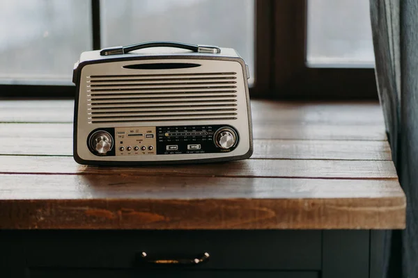 Pencerenin yanındaki ahşap masa yüzeyinde antika bir radyo var. 80 'lere geri dönelim. Müzik nostaljisi ve eski teknoloji konsepti. Antika kaydedici — Stok fotoğraf