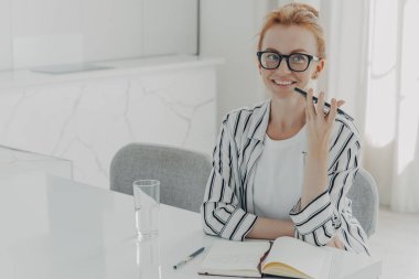 Genç gülümseyen iş kadını akıllı telefonda ses asistanı uygulaması kullanıyor, evde masada oturuyor.