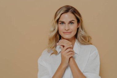 Uzun saçlı, beyaz renkli tişörtlü, düşünceli genç bayan göğsünde katlanmış el ele tutuşuyor.