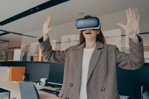 Zaskoczona kobieta doświadczająca niesamowitego świata wirtualnej rzeczywistości z goglami VR w pracy — Zdjęcie stockowe