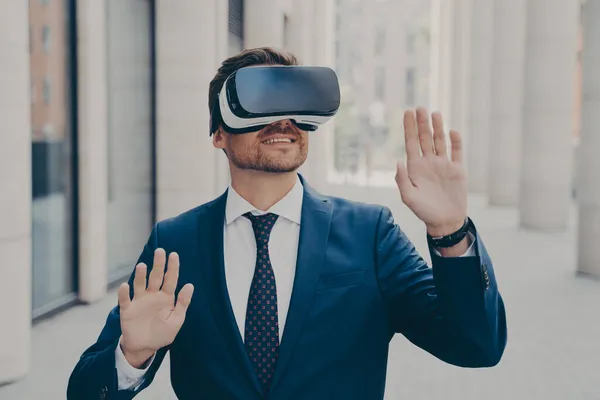 Young excited man in suit standing on city street and testing VR glasses or 3d goggles