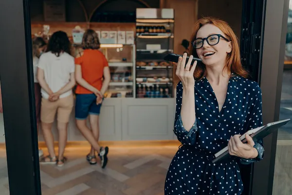 Pelirroja joven mujer hace llamada de voz mantiene teléfono inteligente cerca de la boca lleva gafas vestido de lunares — Foto de Stock