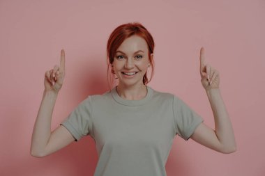 İşaret parmaklarıyla yukarıya doğru işaret eden ve neşeyle gülümseyen mutlu beyaz bir kadın.