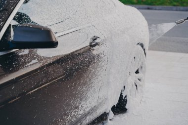 Black luxury car in white snow foam during car wash outdoors clipart