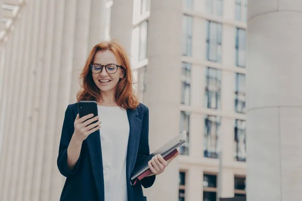 Joven hermosa pelirroja mujer ceo ejecutivo mirando el teléfono inteligente con expresión de la cara emocionada — Foto de Stock